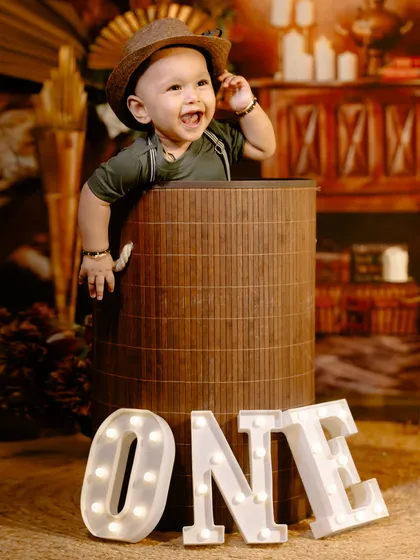 A happy one-year-old pops out of a large basket in this fun, rustic-themed birthday shoot with light-up 'ONE' letters.