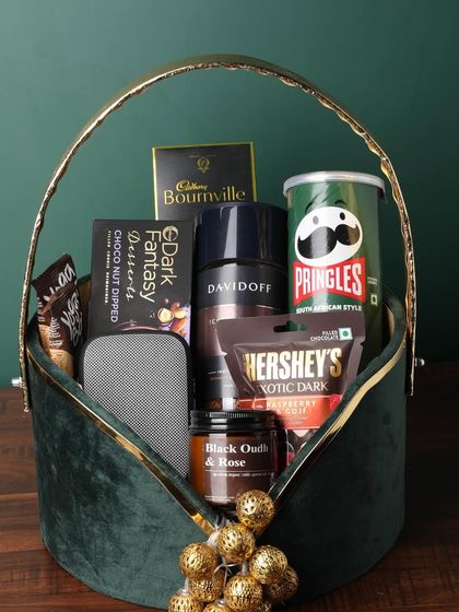 This luxurious green velvet basket is overflowing with premium brands. This hamper includes Davidoff coffee, Pringles, Bournville, Hershey's, a portable speaker, and a black oudh and rose candle.