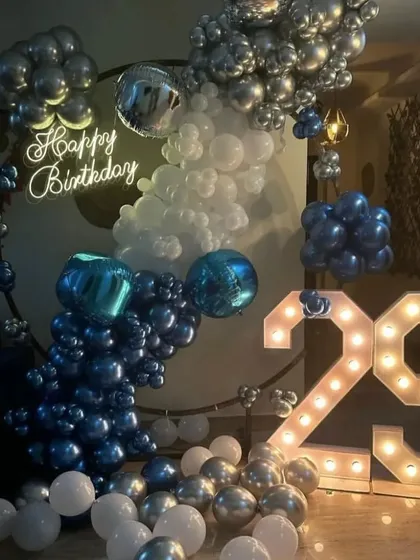 A stylish 29th birthday decoration with a cool blue and silver color scheme. The setup includes a circular balloon arrangement, a neon sign, and a large light-up number '29'.