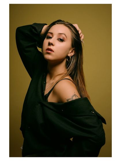 A moody and intense portrait with a dark, olive-green background. The lighting is focused on the model's face, creating a dramatic and captivating image.