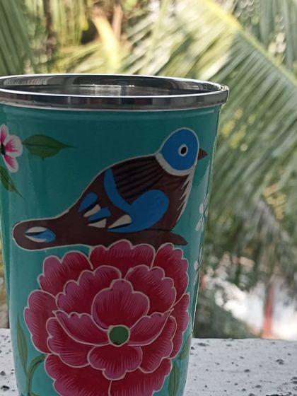 A hand-painted steel tumbler featuring a beautiful bird perched on a flower, set against a tropical background.