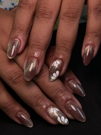 A beautiful example of a brown cat-eye gel polish with delicate, hand-painted white daisy accents. It’s a lovely mix of earthy tones and floral art.