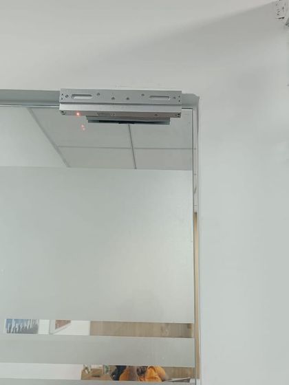 An EM lock installed on a frosted glass door. The red indicator light confirms that the magnetic lock is active and the door is secured.