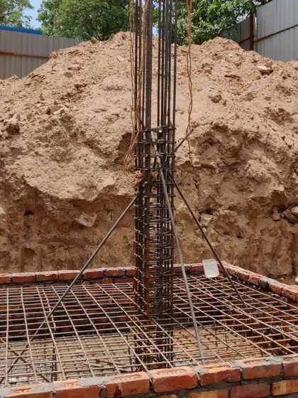 A close-up of a reinforced concrete column rising from the foundation, showing the dense network of steel bars that will give the building its strength.