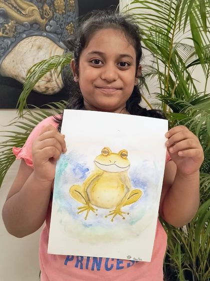 A student proudly presents her wonderful watercolor painting of a friendly yellow frog.