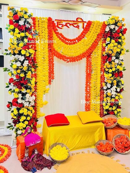 The main backdrop of the Haldi setup, with pillars of red, yellow, and white flowers and hanging marigold garlands.