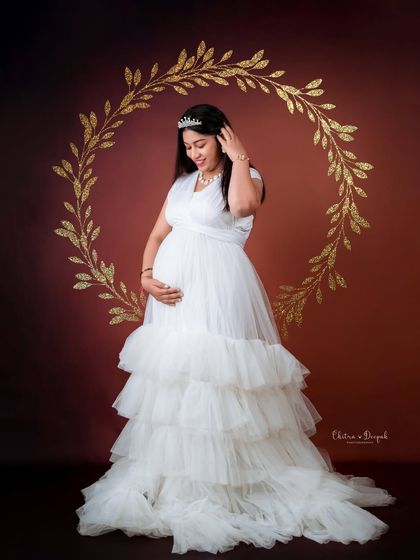 A classic portrait in white. The golden wreath backdrop adds a touch of elegance to this simple and beautiful shot of a mom-to-be in a tiered white gown.