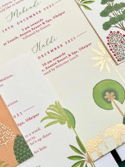 A close-up of the handmade paper invitations, showing the gold foil elephant details. The combination of the rustic paper and the metallic foil creates a stunning contrast.