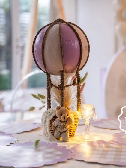 The full hot air balloon centerpiece, complete with a miniature basket and teddy bear passenger, illuminated by a soft light.