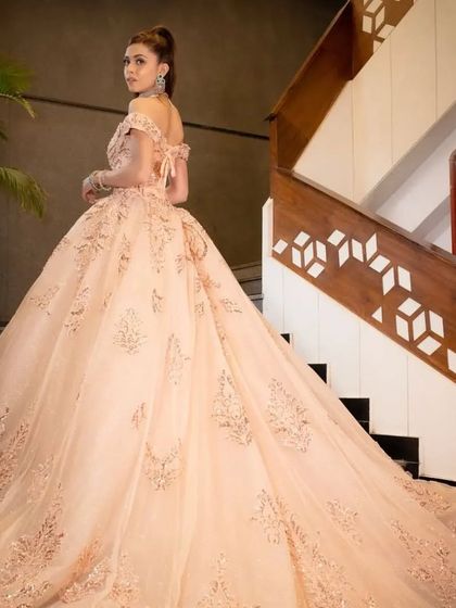 The back view of the peach ball gown, highlighting its long, flowing train and lace-up corset detail, ensuring a perfect fit.