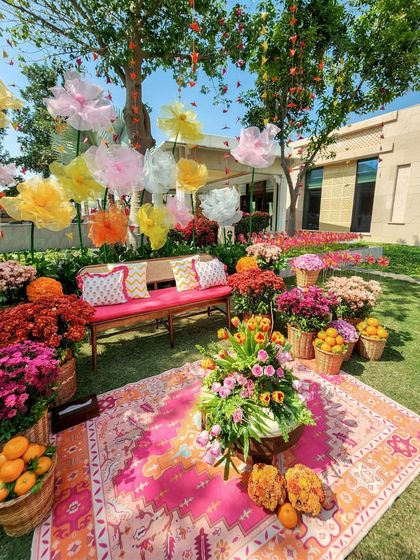 A beautiful photo spot we created for the garden Mehendi. The setup includes a plush bench, a vibrant rug, and an abundance of fresh flowers and citrus fruits in woven baskets.