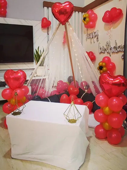 A cozy floor seating arrangement for an intimate birthday celebration. I created a teepee-style canopy with fairy lights, surrounded by red heart-shaped foil balloons and balloon bunches.
