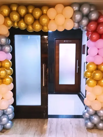 A classic balloon arch over a doorway using a mix of gold, silver, peach, pink, and red balloons. This is a versatile decoration for any kind of event.