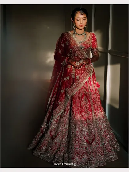 A bride in her magnificent red lehenga, caught in a dramatic play of light and shadow. This is bridal portraiture as art.