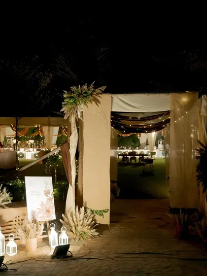 The entrance to the bohemian-themed party, decorated with pampas grass, white lanterns, and a personalized welcome sign.