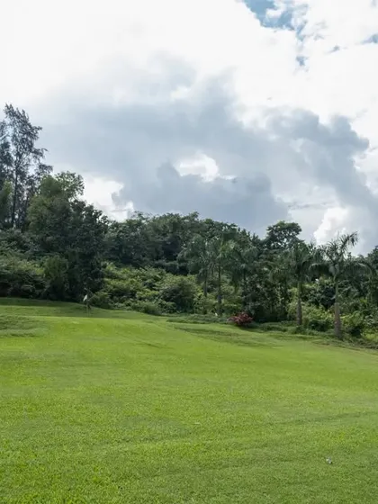 A golf cart sits on the edge of a wide, rolling fairway, with the lush, tree-covered hills in the background. This image shows the scale and natural beauty of our expansive course.