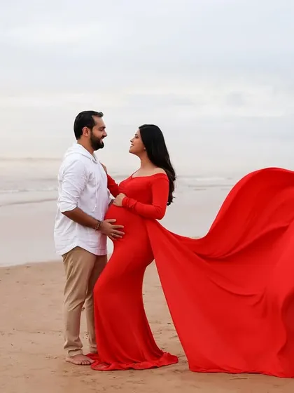 A romantic moment by the sea. The couple shares a look of love as the wind catches her vibrant red gown, creating a dynamic and beautiful portrait.