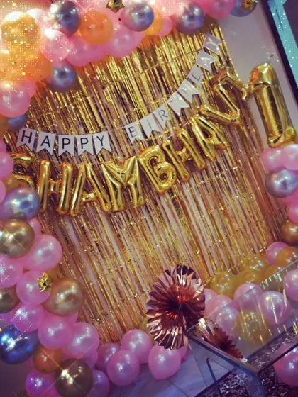 A close-up of a pink and gold themed decoration, showing foil letter balloons against a gold shimmer curtain.