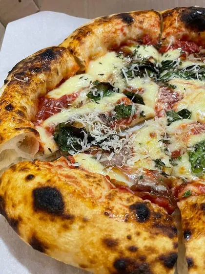 A beautiful pizza with a perfectly puffed cornicione. The slice is pulled away to show the light, open structure of the crust, a testament to the dough's long fermentation.