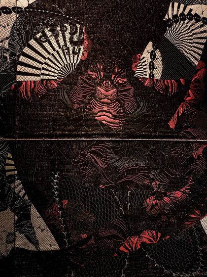 A detailed close-up of the 'Gothilicious' textile. The design, inspired by tattoo art, features intricate patterns in black, grey, and red, projecting a bold and glamorous persona.