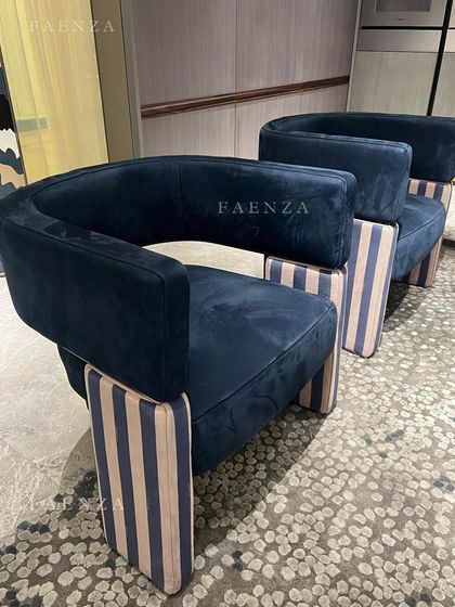 A bold and graphic armchair design. The chair features a deep blue velvet upholstery, a curved back, and distinctive striped block legs, making it a piece of functional art.
