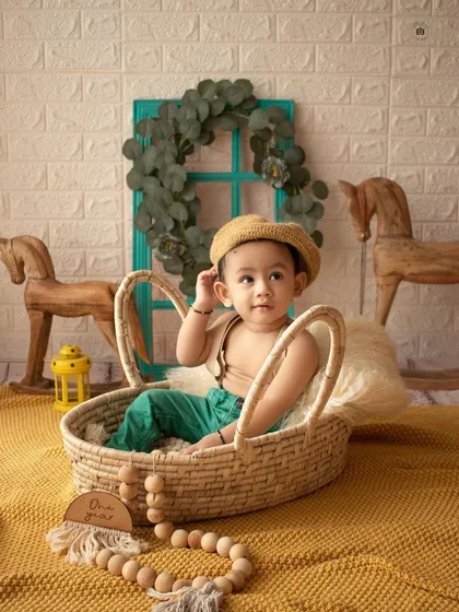 A charming setup with a baby boy in a wicker basket, surrounded by wooden horses and a warm yellow blanket.