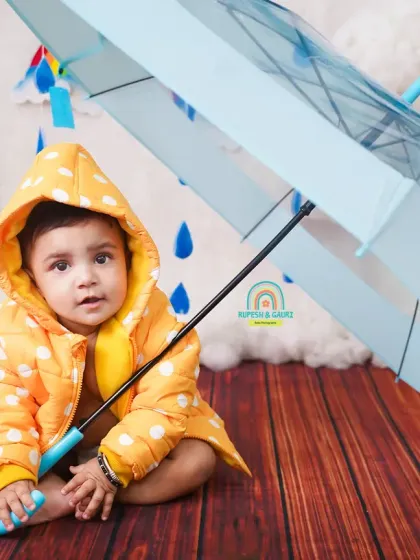 A curious baby in a yellow raincoat holds an umbrella in our adorable monsoon setup. These seasonal mini-sessions are a fun way to capture milestones.