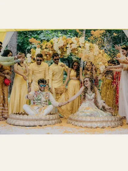 A picture of pure fun from the Haldi ceremony. The couple sits together, holding hands, as their friends and family shower them with flower petals, creating a vibrant and joyful memory.