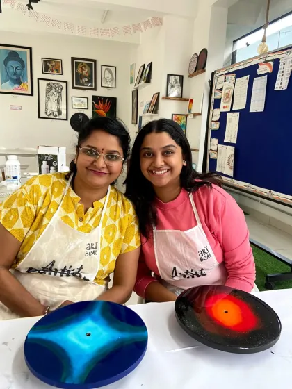 Two friends proudly display their unique resin clock designs, one with a blue swirl and the other a fiery galaxy pattern.