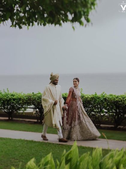 The couple takes a stroll along a garden path by the sea. This wide shot captures the beauty of the location and the quiet elegance of the couple on their wedding day.