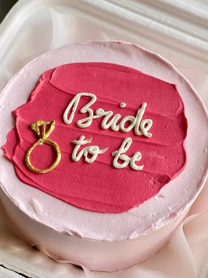 A "Bride to be" bento cake in shades of pink, complete with a hand-piped engagement ring. It's a fun and sweet way to celebrate an upcoming wedding.