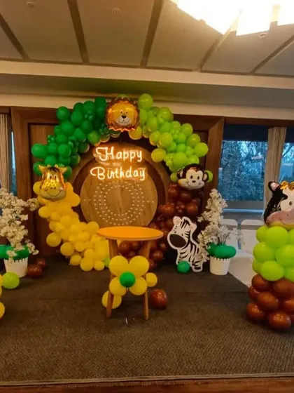A vibrant jungle animal theme with a neon 'Happy Birthday' sign. This setup includes balloon columns topped with animal head foil balloons like a tiger, giraffe, zebra, and cow.
