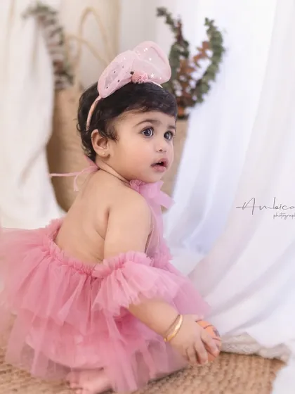 A sweet glance over the shoulder. This baby girl looks adorable in her pink tulle romper, a perfect outfit for a first birthday celebration.