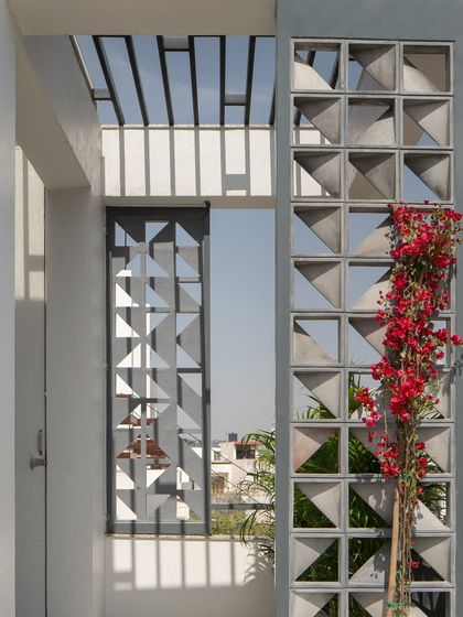 The modular facade, with its triangular voids, creates a beautiful play of light and shadow. A bougainvillea vine adds a splash of color to the grey concrete, softening the geometric design.