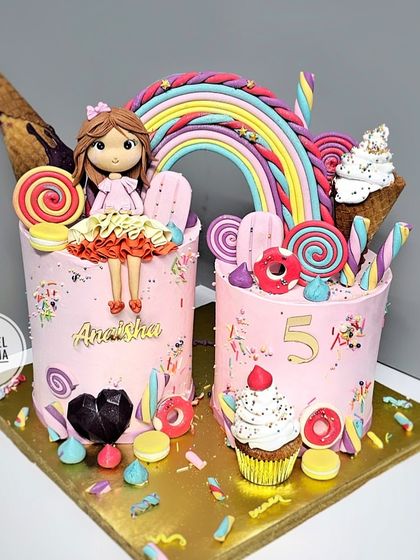 Welcome to Candyland. This vibrant creation features two cakes loaded with sweet treats like lollipops, macarons, ice cream cones, and a rainbow, with a custom figurine of the birthday girl.