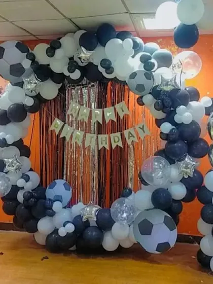 A football-themed ring backdrop in black and white. The setup includes a silver fringe curtain, football balloons, and a large number '8' foil balloon.