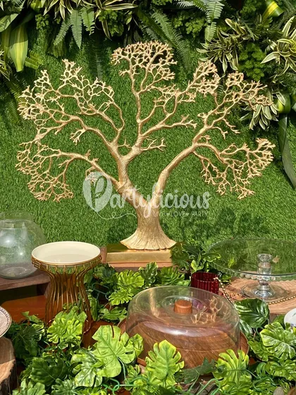 A close-up of the dessert table at a jungle-themed party, featuring a golden tree-of-life centerpiece against a lush green backdrop.