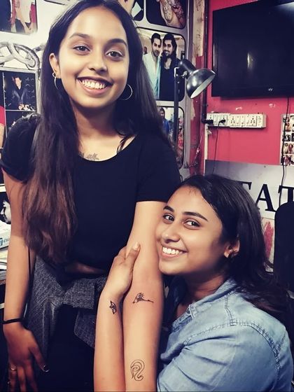 Two friends smiling and showing their matching minimalist tattoos.