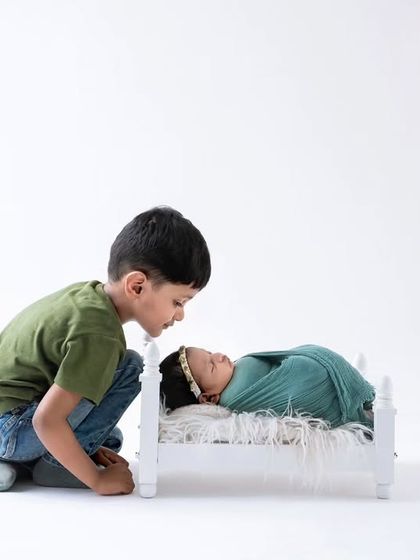 An older brother curiously looks at his new baby sister sleeping in a miniature bed. This shot captures the natural curiosity and start of a new sibling relationship.