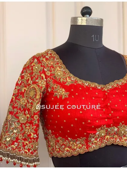 The front of the red bridal blouse, featuring a sweetheart neckline and scattered pearl embellishments. The sleeves and neckline are heavily embroidered with gold zardozi work.