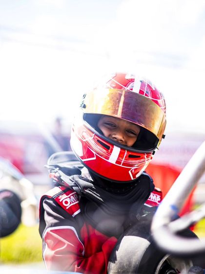 A young driver in his red race suit, smiling and ready to go.