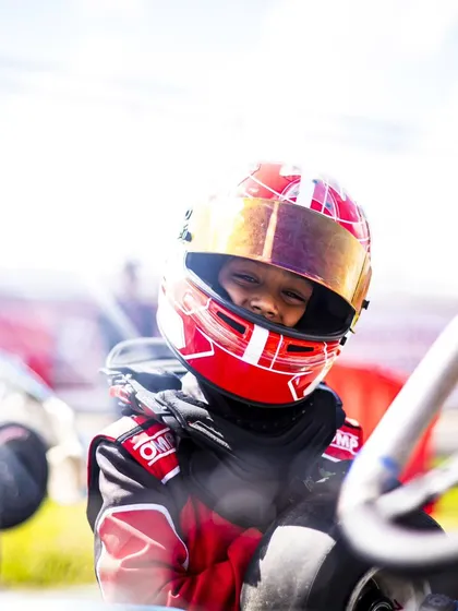 A young driver in his red race suit, smiling and ready to go.