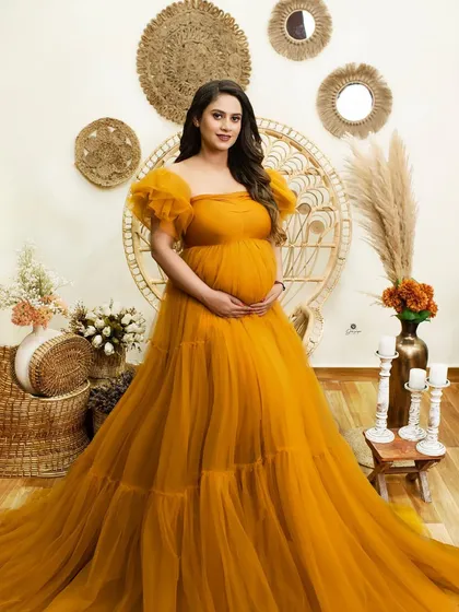 A full-length portrait in a flowing mustard yellow gown, set against a rustic, bohemian-inspired backdrop. The client's radiant smile completes this cheerful and stylish shot.