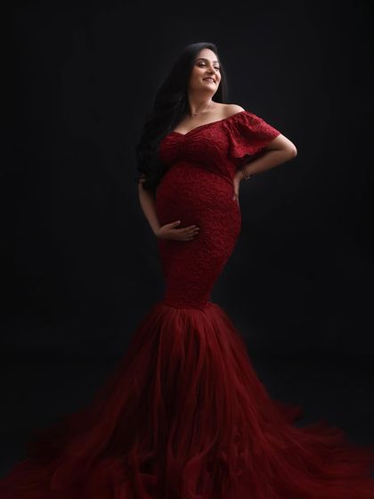 A joyful and radiant portrait. The mom-to-be's happy expression and the stunning red gown combine to create an image that is full of life and energy.