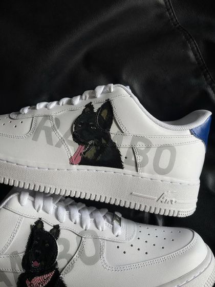 A close-up of a custom Nike Air Force 1 featuring a portrait of a black dog named Rambo.