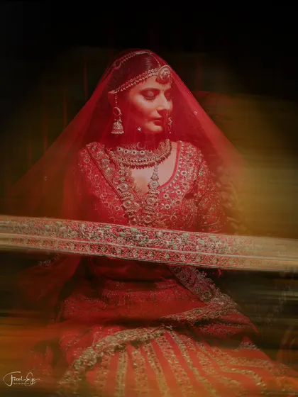 An artistic bridal portrait using motion blur to create a dynamic and abstract feel. The focus remains on the bride's serene face amidst the blur of her red lehenga.
