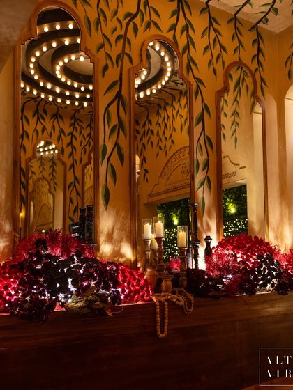 Hand-painted details by local artists adorned the walls at our 'Mid-Century Mod' event. This corner features deep red florals against a backdrop of painted vines and mirrored arches, creating a warm and tranquil space.