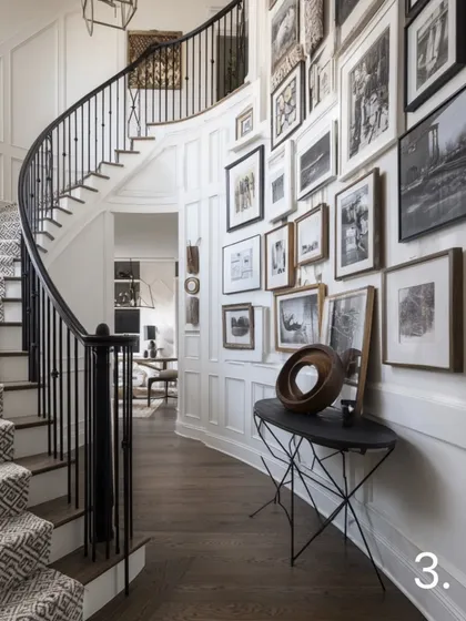 Achieve a striking, elegant look with monochrome magic. This gallery wall along a curved staircase uses a dense collection of black-and-white photos in varied frames, creating a dramatic and classic statement against the white wall paneling.