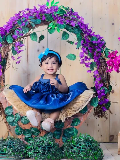 A happy and engaging portrait of the baby girl in blue, smiling and looking directly at the camera.