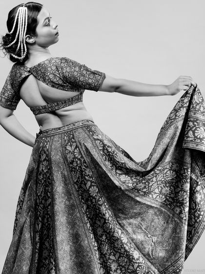 A graceful black and white portrait showing the back of a lehenga blouse and the flow of the skirt. This artistic shot focuses on the design and movement of traditional Indian attire.